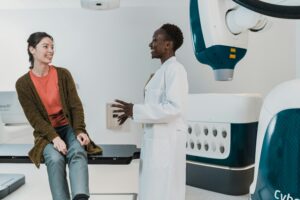A patient smiling and talking with her doctor beside a radiation therapy machine before treatment.