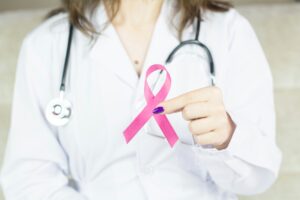 An Abarca Health doctor in a white coat holding a pink awareness ribbon, symbolizing breast cancer awareness.