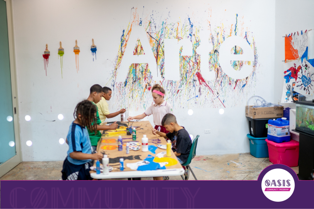 Children from The Boys & Girls Club painting together at a table in an art space, with a colorful wall mural behind them, supporting creativity and leadership development.