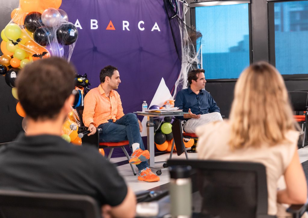 Jason Borschow and Ricardo Álvarez-Díaz speaking during an Oasis Connections session at Abarca Health, with Halloween-themed decorations in the background