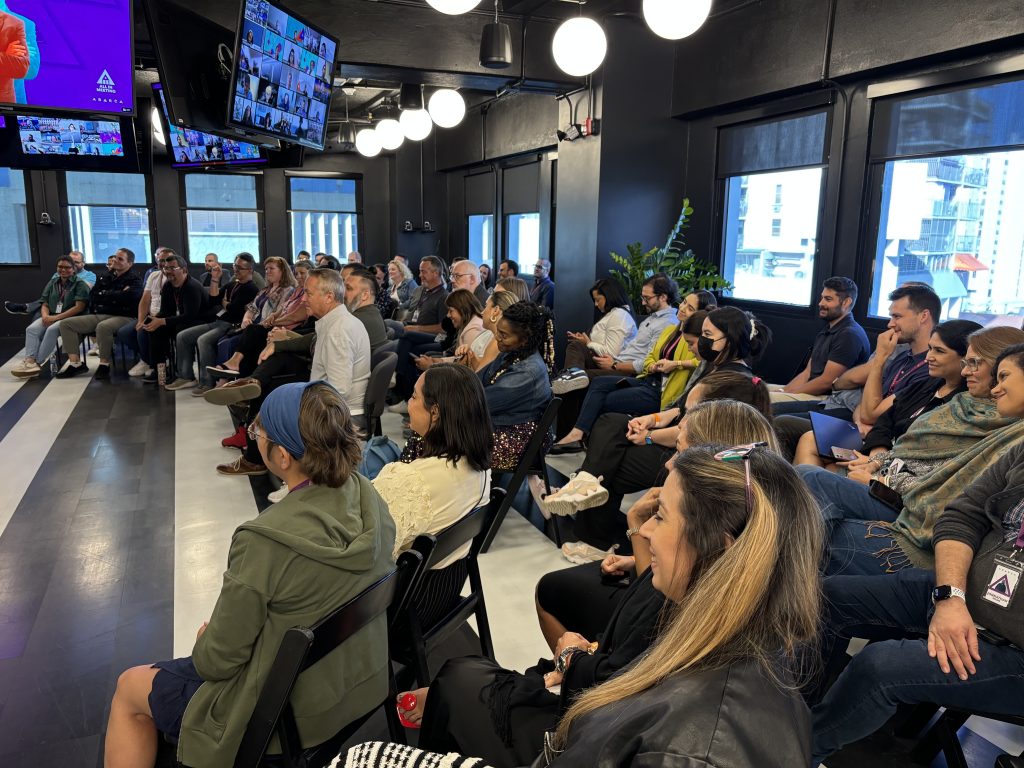Audience of professionals attentively listening to the panel discussion during an Oasis Connections leadership session at Abarca Health’s Oasis Santurce campus, with virtual participants visible on screens