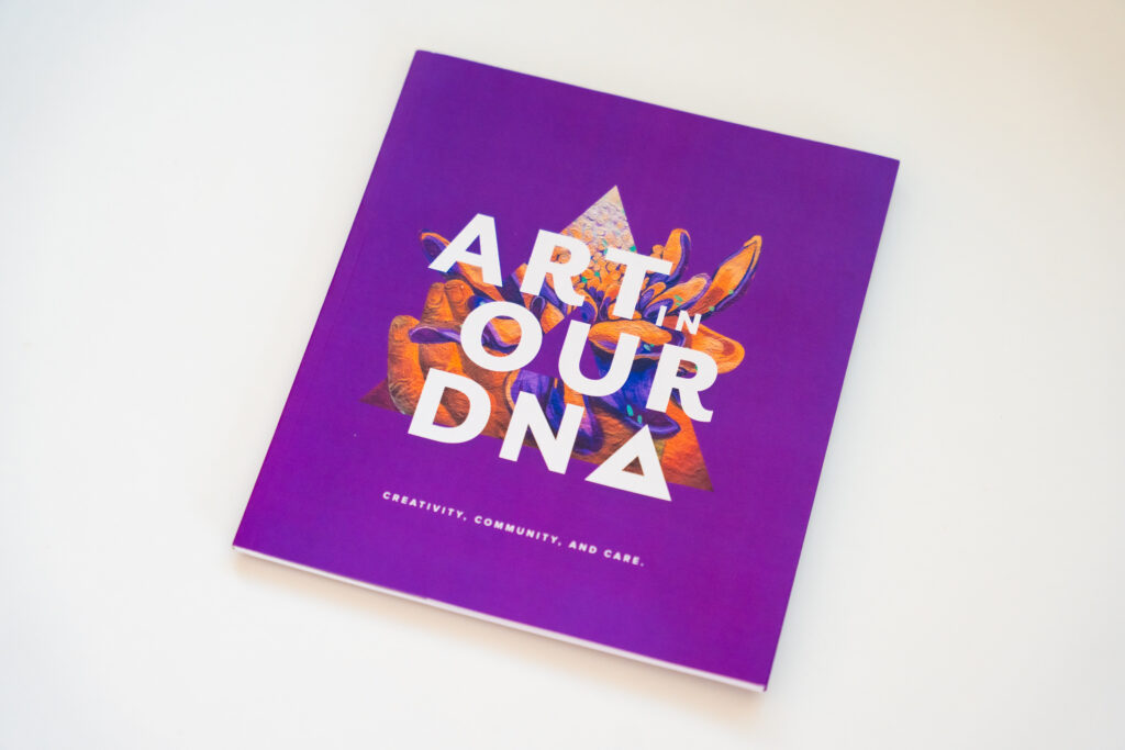 Square booklet created by Abarca Health featuring a vibrant purple cover with layered, colorful abstract artwork behind bold white text that reads “ART IN OUR DNA,” with smaller text below stating “Creativity, community, and care.