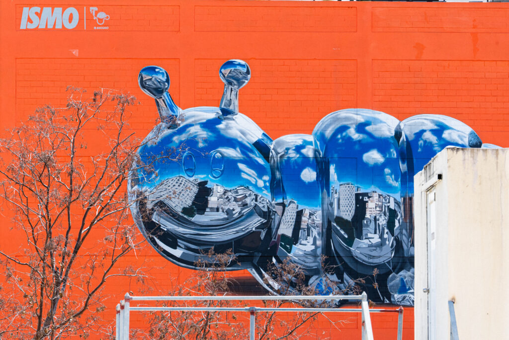 Bikismo’s chrome caterpillar mural, reflects Santurce’s urban landscape on Abarca Health’s bright orange façade.